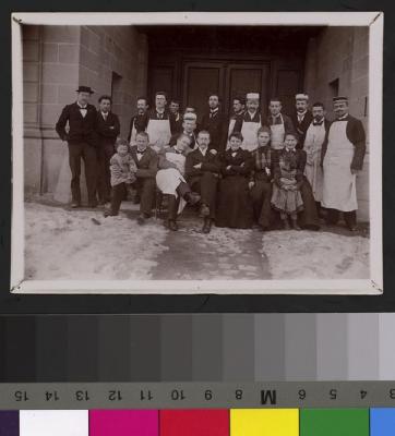 Volée d'étudiants avec leurs professeurs sous le porche de l'Ecole de médecine. On reconnaît, a gauche de l'image, les mains dans les poches et chapeau sur la tête, le professeur Henri Preisig. Quelques portraiturés portent la casquette de leur société…