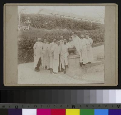 Portrait d'un groupe de médecins dans un parc. De droite à gauche: Dr Charlotte Olivier, Dr André Guisan (3e) et Dr Paul Vuilleumier (6e). A l'arrière plan, une sorte de pavillon.